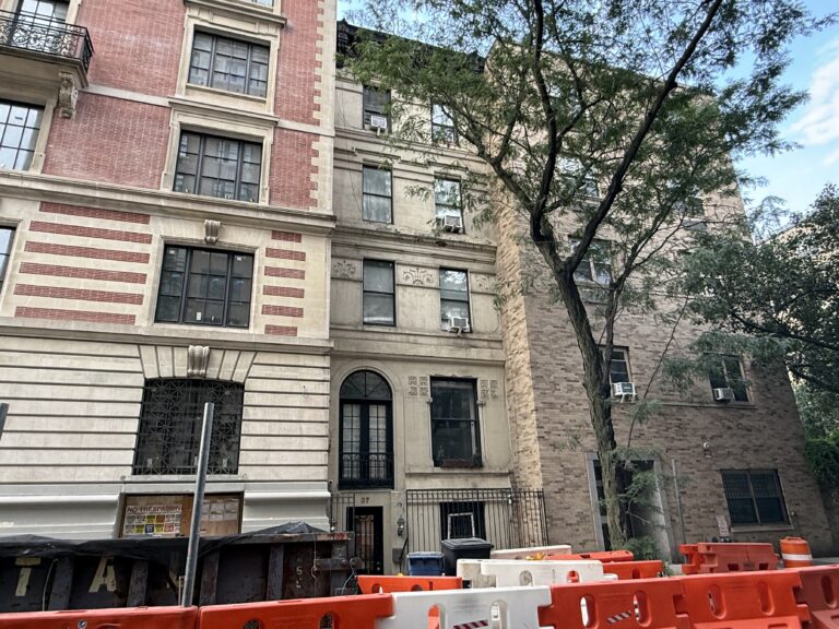 Image shows a skinny townhouse on a city block.