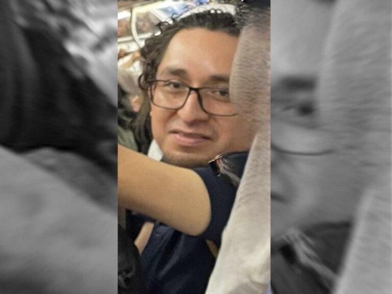 Image shows a man with dark hair and glasses on a subway train.