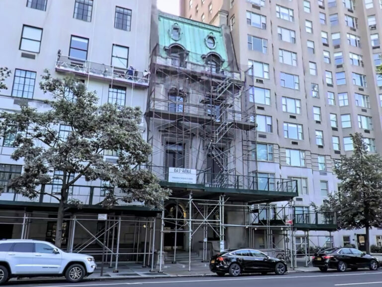 Image shows a mansion between apartment buildings with scaffolding in front.