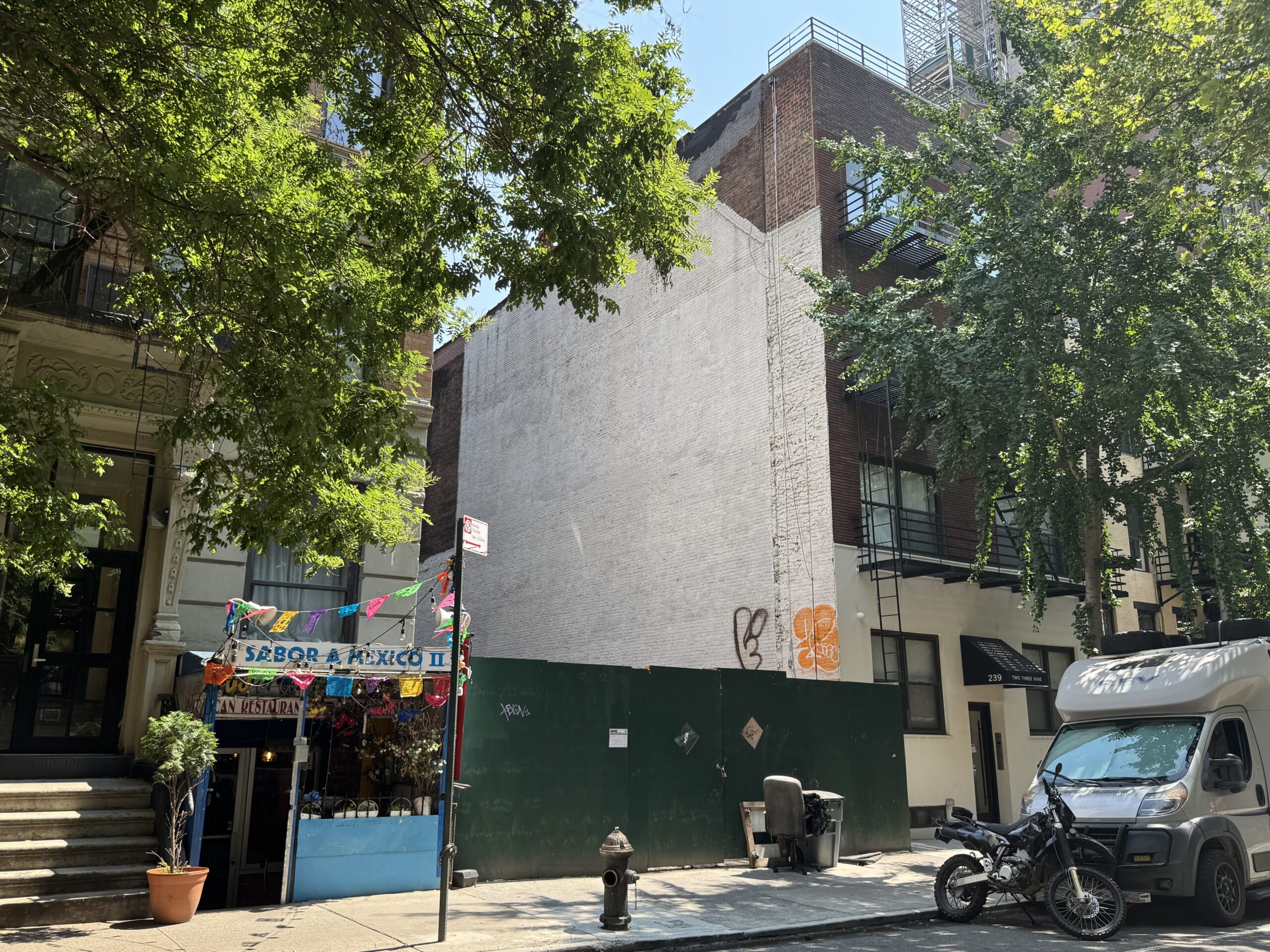 Photo shows a vacant lot between low-rise buildings backed by a green construction fence.