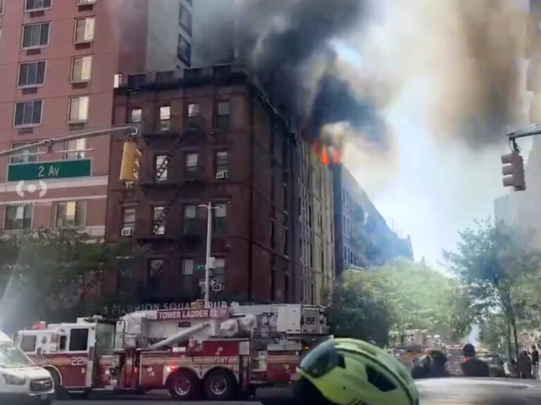 Image shows a fire burning on the roof of a low-rise apartment building in New York City.