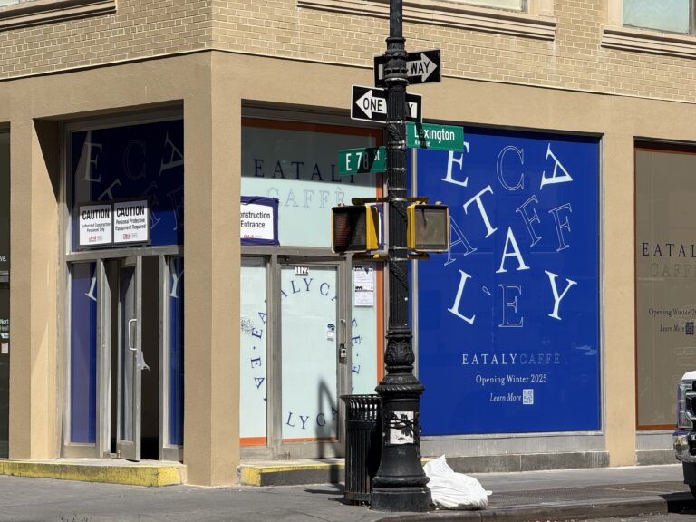 Photo shows beige corner building with blue signage covering the windows advertising "Eataly."