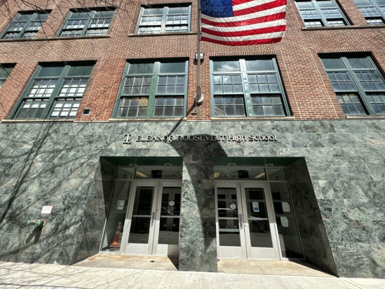 Photo shows a red brick school with an entrance clad in polished stone tile. An American flag flies above the doors.
