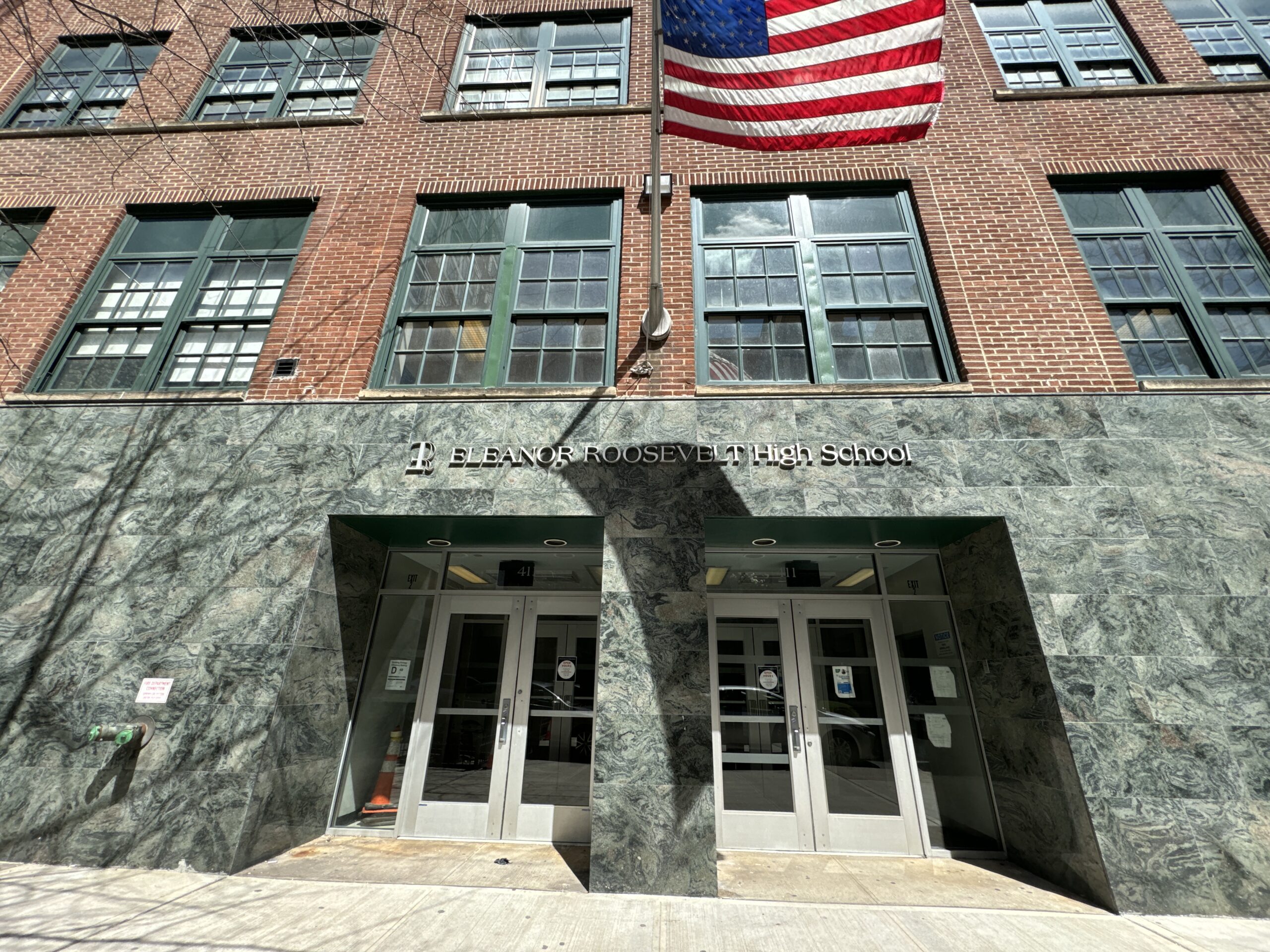 Photo shows a red brick school with an entrance clad in polished stone tile. An American flag flies above the doors.
