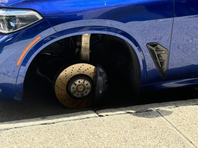 Photo shows a blue SUV with a front wheel stolen off.