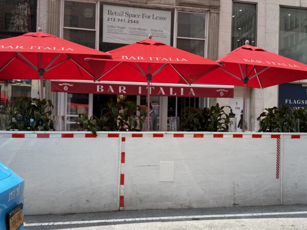 Photo shows a dirty white outdoor dining structure with red umbrellas standing over it.