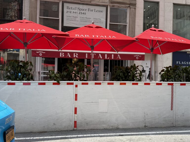 Photo shows a dirty white outdoor dining structure with red umbrellas standing over it.