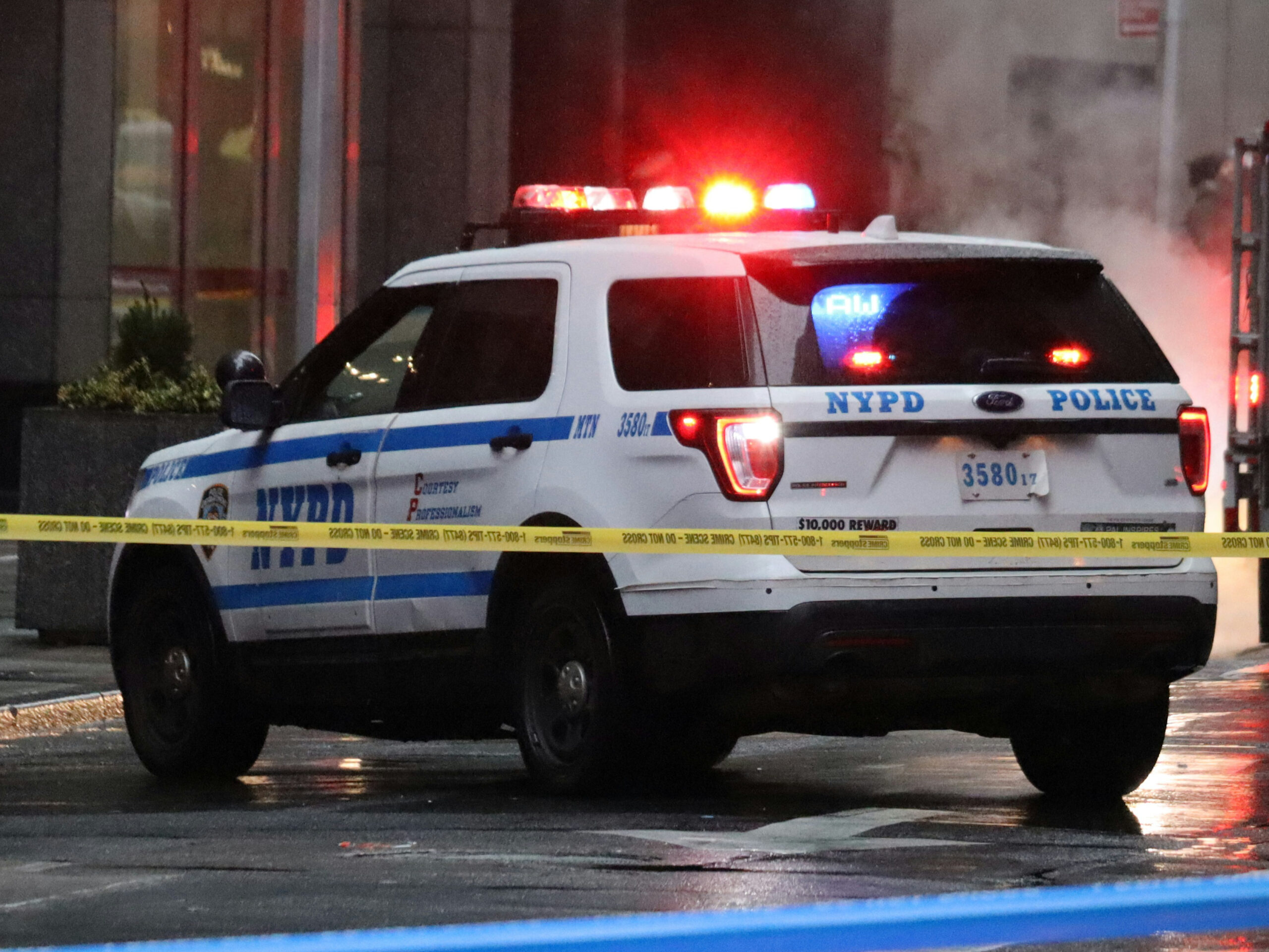 Photo shows a police SUV with its emergency lights on behind police tape.