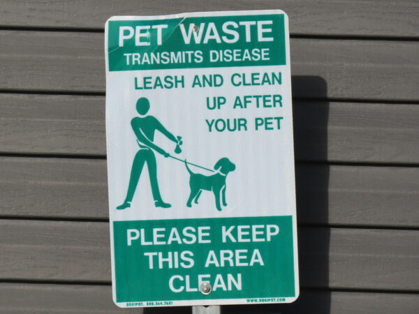 Photo shows a green and white sign instructing dog owners to clean up pet waste.