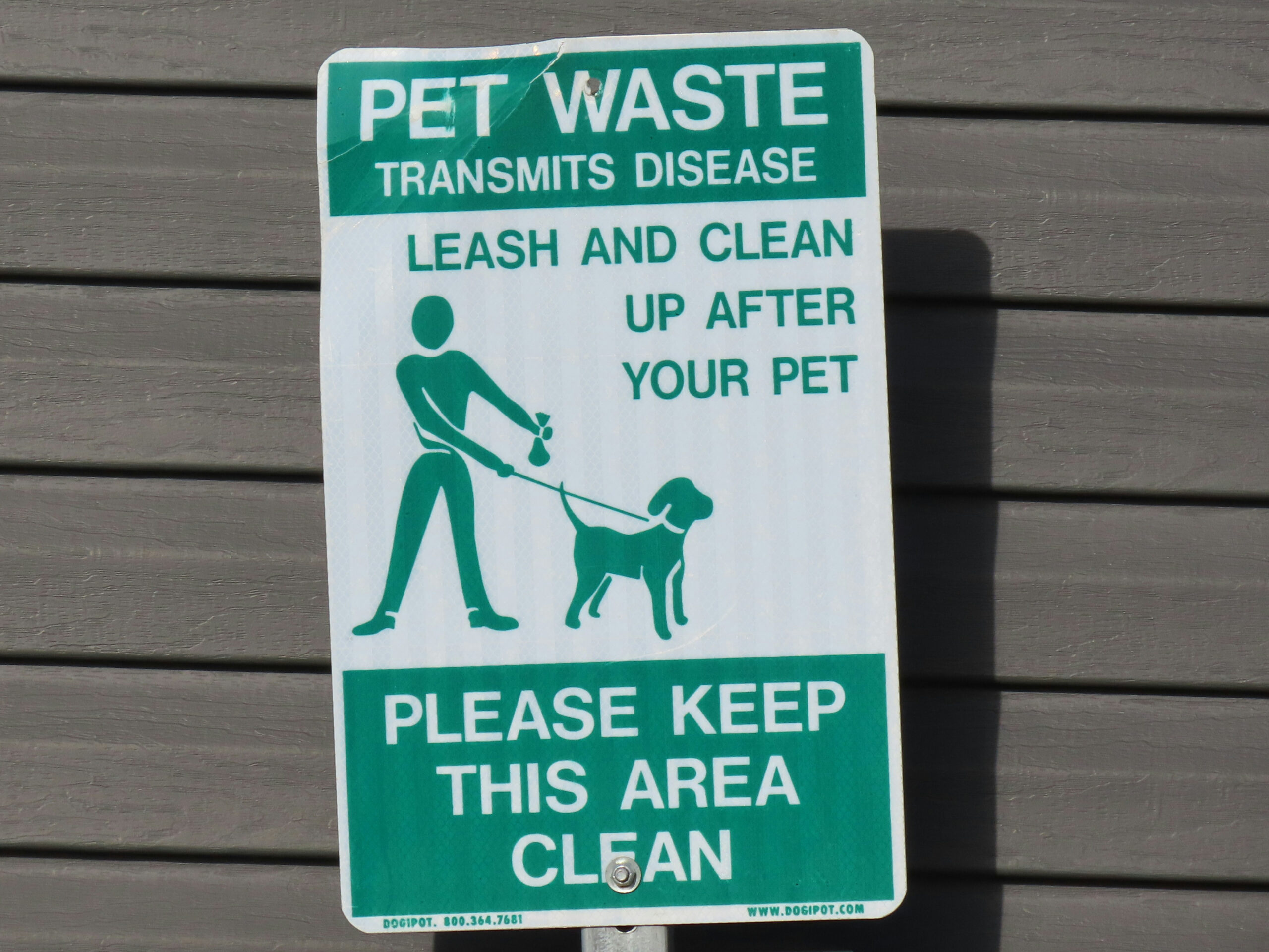 Photo shows a green and white sign instructing dog owners to clean up pet waste.